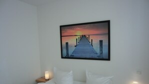 A hotel room with a bed, white bedding, a sunset painting, and bedside lamps. - 3-zimmer-fewo für 4 Pers. im 1. OG (Graal-Müritz)