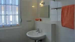 Casa de banho com lavatório branco, espelho, porta-toalhas e janela com persianas.