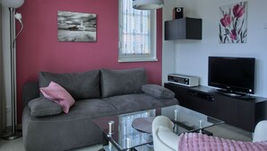 Uma sala de estar moderna com sofá cinza, mesa de centro de vidro, televisão de tela plana e uma parede em destaque vermelha.