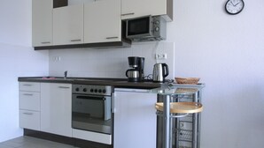 Uma cozinha compacta com armários brancos, micro-ondas, cafeteira e pequena geladeira.
