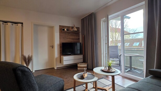 A modern living room with a flat-screen TV, grey sofas, a small round table, and a sliding glass door leading to a balcony. - 2-zi.-fewo im 2. OG, ca. 45 m² für 4 Personen mit Wlan (Graal-Müritz)