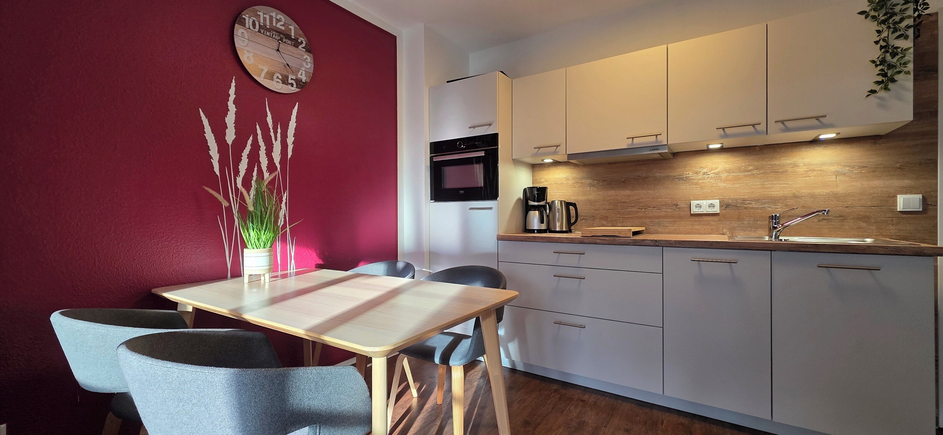 Una cucina moderna con un piano di lavoro in legno, mobili bianchi e una parete decorata di rosso.