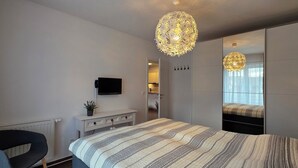 A modern bedroom with a large bed, a desk, a chair, a TV, and a chandelier. - 2-zi.-fewo im 2. OG, ca. 45 m² für 4 Personen mit Wlan (Graal-Müritz)