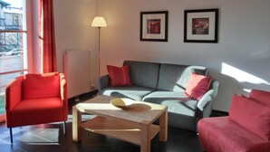 A living room with a grey sofa, red armchair, and a wooden coffee table. There are two framed pictures on the wall and a floor lamp. - 2-zi.-fewo für 4 Personen im 2. OG (Graal-Müritz)