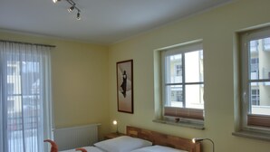 A hotel room with a large bed, two bedside tables, a nightstand, a window with blinds, and a ceiling light fixture. - 2-zi.-fewo für 4 Personen im 1. OG mit Wlan (Graal-Müritz)