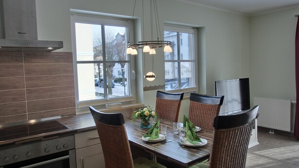 A modern kitchen with a dining area, large windows, and a built-in oven. - 2-zi.-fewo für 4 Personen im 1. OG mit Wlan (Graal-Müritz)
