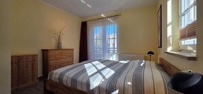 A bedroom with a bed, a dresser, a radiator, a window with blinds, and a lamp.