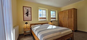 A bedroom with a bed, bedside lamps, a wooden wardrobe, and two windows with blinds. - 2-zi.-fewo für 4 Personen im 1. OG mit Wlan (Graal-Müritz)