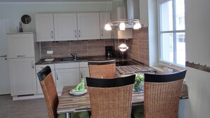 A modern kitchen with white cabinets, a built-in oven, a coffee maker, and a dining area with wicker chairs and a wooden table. - 2-zi.-fewo für 4 Personen im 1. OG mit Wlan (Graal-Müritz)