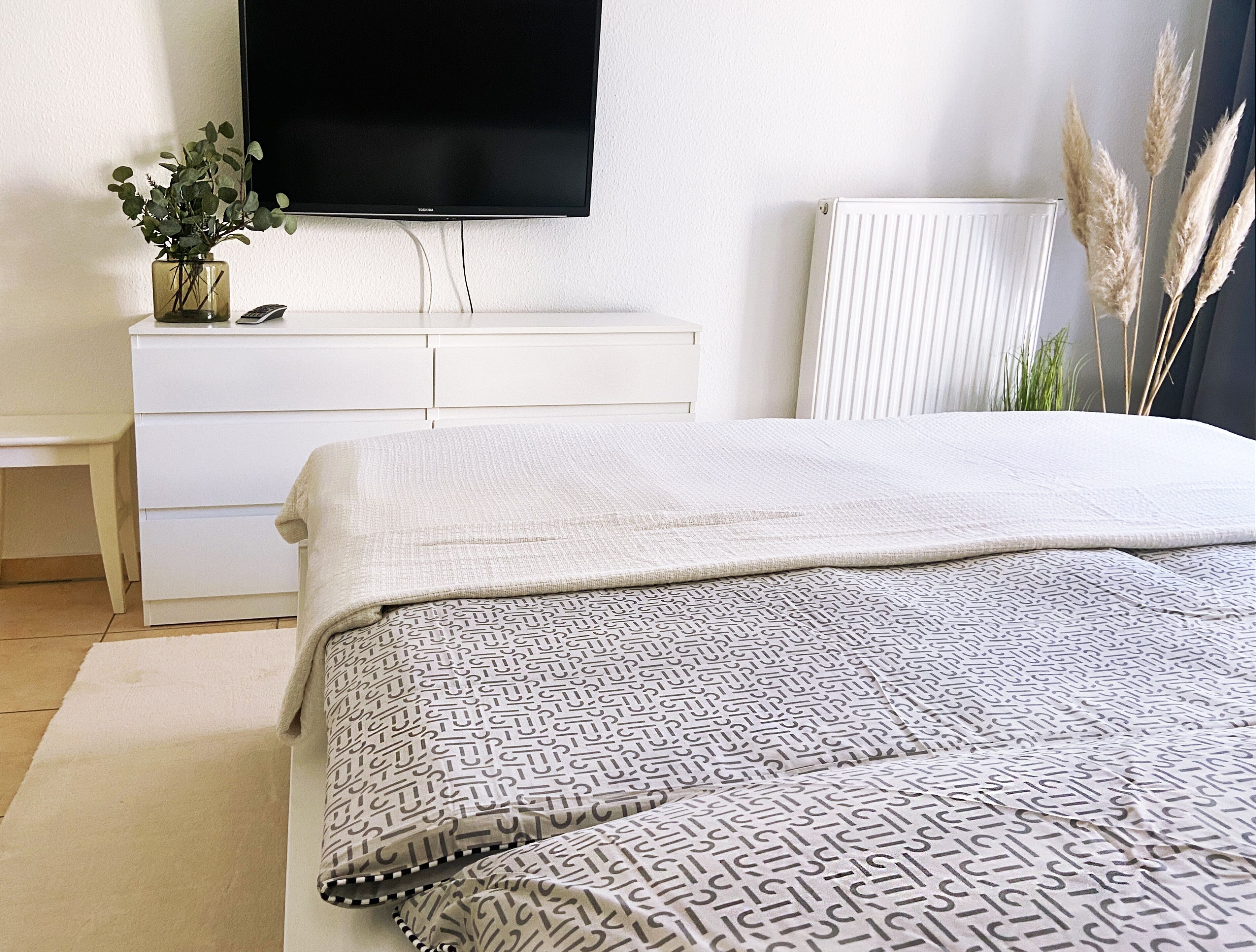 Un dormitorio con cama, cómoda, televisor y radiador.