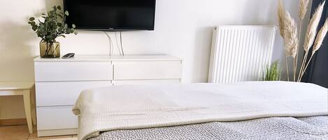 Un dormitorio con cama, cómoda, televisor y radiador.