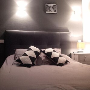A bed with a dark headboard and two patterned pillows, a bedside table with a lamp, and a framed picture on the wall. - Chez l'ahumat (Aire-sur-l'Adour)