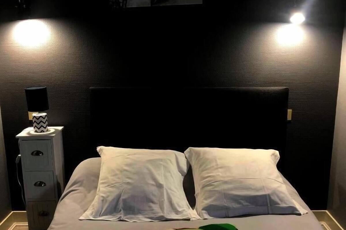 A bed with white pillows, a colorful pillow, a headboard, and a nightstand with a lamp.