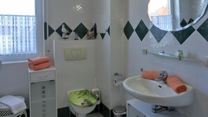 Baño con inodoro, lavamanos y espejo. Se ve una ventana con vistas a edificios.