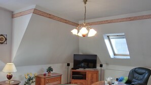 Una sala de estar con un televisor de pantalla plana, un mueble de madera, un sofá de cuero negro, una mesita con una tetera y un jarrón con flores.