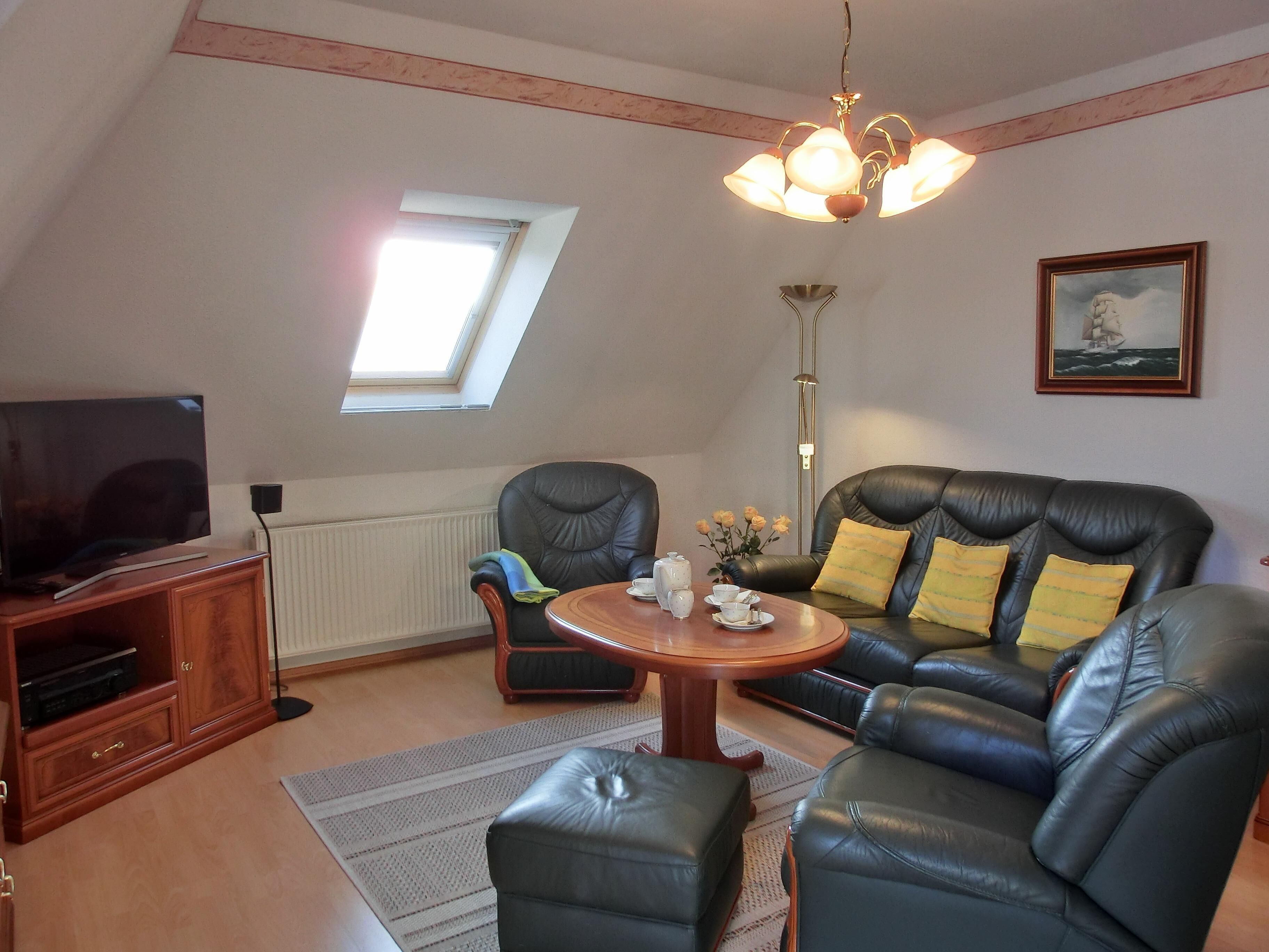 Ein gemütliches Wohnzimmer mit Fernseher, Ledersofa und einem kleinen runden Tisch.