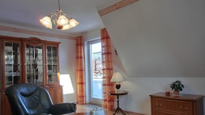 Una habitación con una mesa de comedor dispuesta para té, un sillón de cuero, un aparador con puertas de cristal, una lámpara y una planta en maceta.