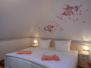 A neatly made bed with white linens and pink towels, a wall with a floral mural, and bedside lamps on a nightstand.