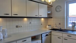 Una cocina con armarios blancos, lavavajillas, fregadero y un reloj en la pared.