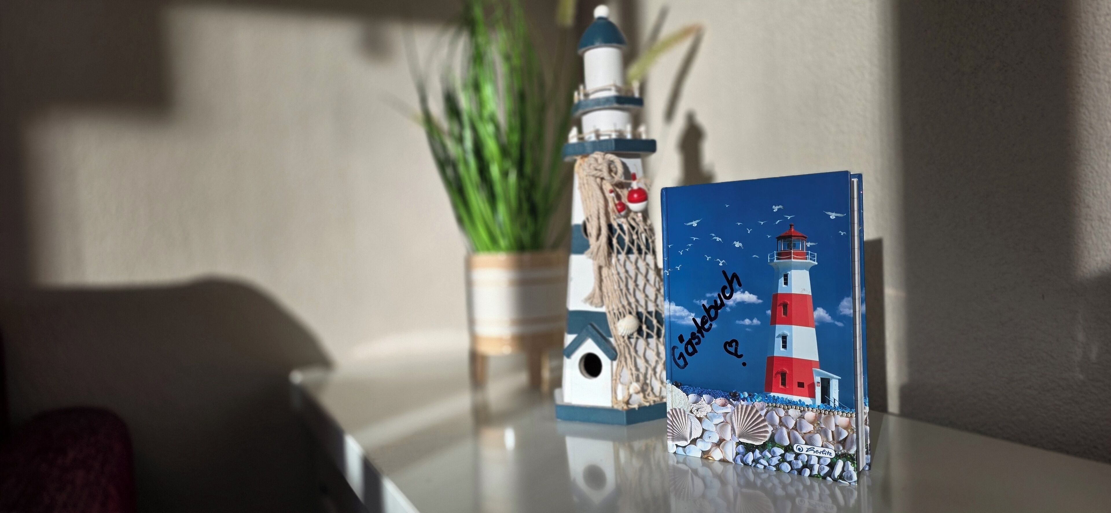Una card a tema faro con un’illustrazione di un gabbiano, posizionata su una superficie riflettente vicino a una piccola pianta e un oggetto decorativo simile a un faro.