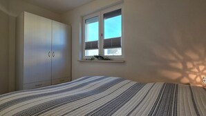 Ein Schlafzimmer mit Bett, Kleiderschrank, einem Fenster mit Jalousien und einer Wandleuchte.