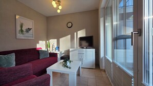 Ein Wohnzimmer mit einem roten Sofa, einem weißen Tisch, einem Fernseher und einer Schiebetür aus Glas.