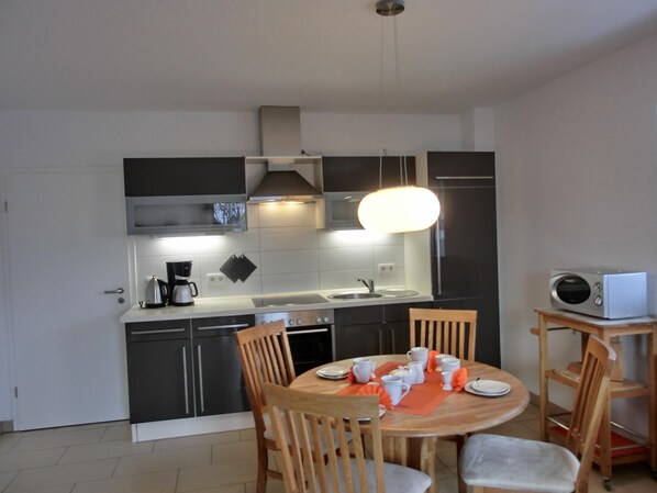 A modern kitchen with dark cabinets, a central island, and a dining area with wooden chairs and a table set for four.