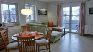 A modern living room with a dining area, large windows, and a view of the outside.