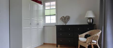 A bedroom with a bed, a dresser, a chair, a window, and a heart-shaped decoration on the wall.