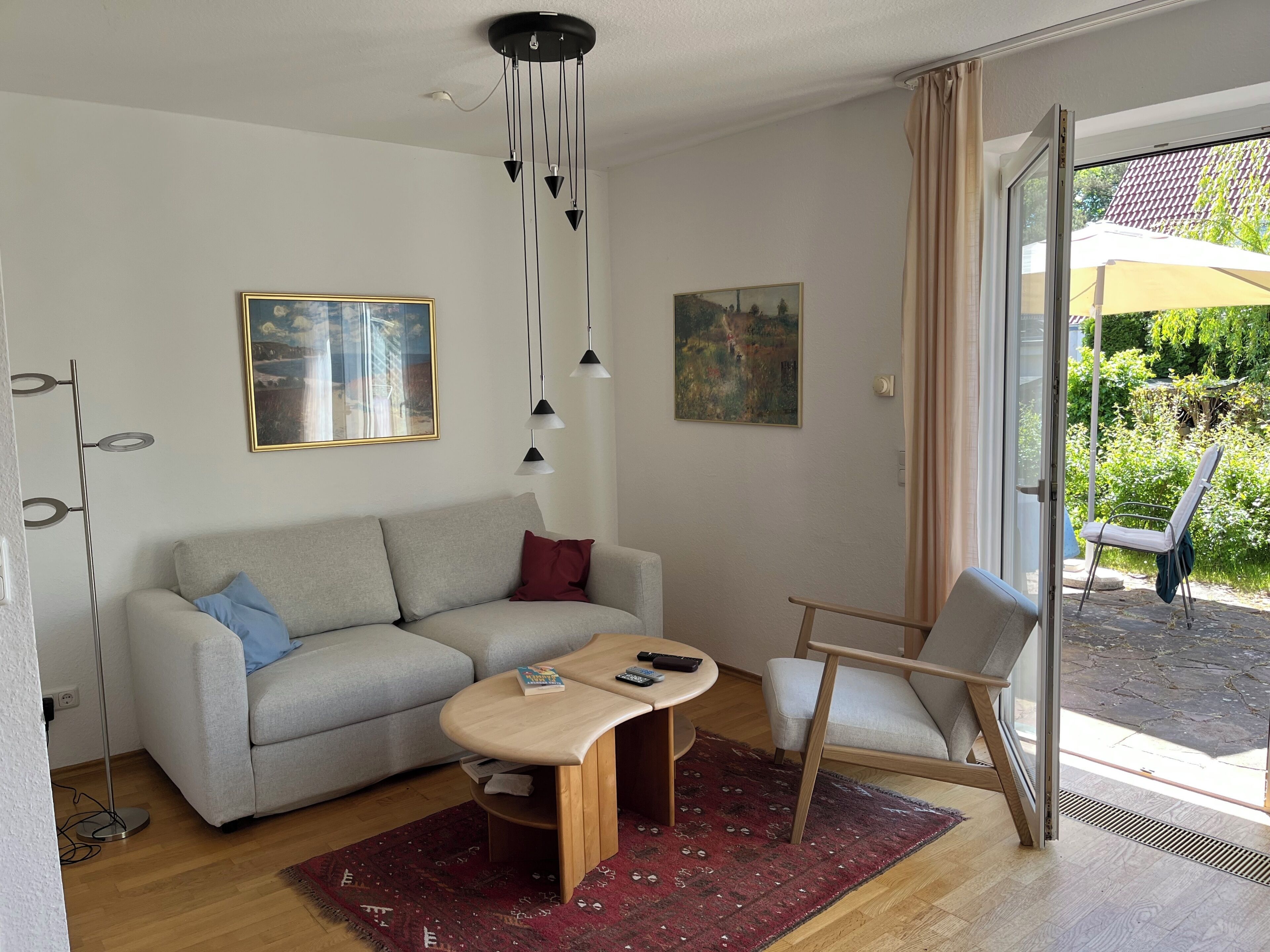 A modern living room with a sofa, coffee table, and chair, a painting on the wall, and a view through a glass door.