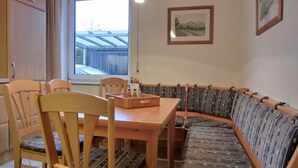 A dining area with a wooden table and chairs, a sofa with patterned cushions, and a window with a view of a wooden deck. - 3-zi.-fewo in Angenehmer und Ruhiger Lage im Erdgeschoss für 6 Pers (Graal-Müritz)