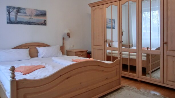 A bedroom with a wooden bed, a nightstand, a mirror cabinet, and a painting on the wall. - 3-zi.-fewo in Angenehmer und Ruhiger Lage im Erdgeschoss für 6 Pers (Graal-Müritz)