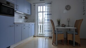 Une cuisine avec des meubles de rangement bleus, une table à manger avec des chaises en osier et une horloge au mur.