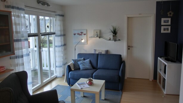 Un salon avec un canapé bleu, une petite table, un téléviseur et une fenêtre avec des rideaux.