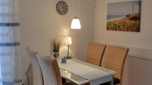 Un espace repas comprenant une table, des chaises, une horloge murale, une lampe suspendue et un tableau.