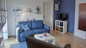 Un salon avec un canapé bleu, une table basse blanche et un téléviseur posé sur un meuble blanc.