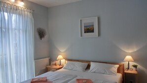 Une chambre d’hôtel avec deux lits, du linge de lit blanc, un tableau encadré au mur et deux lampes de chevet.