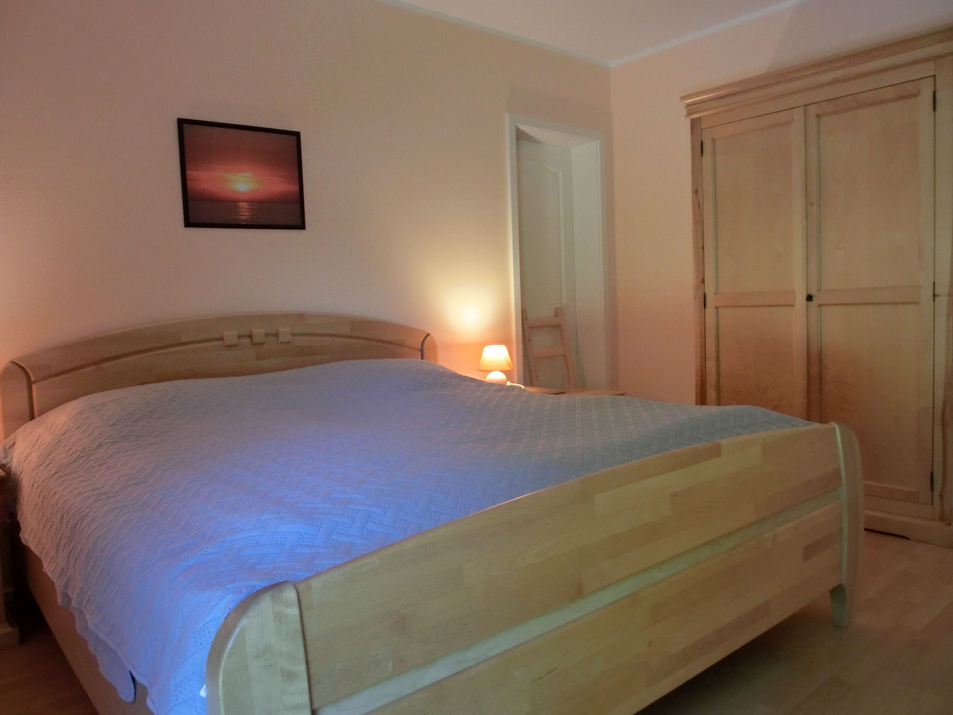 Un dormitorio con una cama de madera, una mesita de noche con una lámpara, un armario y un cuadro enmarcado en la pared.