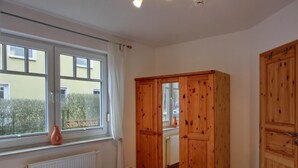 Une chambre avec deux lits, une armoire en bois, une fenêtre donnant sur l’extérieur et un radiateur.