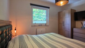Een slaapkamer met een bed, een raam, een radiator, een kledingkast, een dressoir en een televisie.