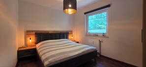 A bedroom with a bed, two bedside lamps, a window, and a radiator.