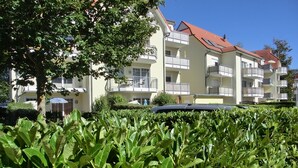 Een meerlaags gebouw met balkons, een dak met rode tegels en een verzorgde tuin op de voorgrond.
