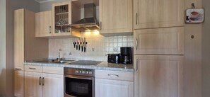 A kitchen with light wood cabinets, a stainless steel range hood, a double sink, a coffee maker, and a toaster. - 2-room apartment for max. 2 pers. with balcony on the 1st floor (Graal-Müritz)