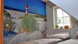 Ein Schlafzimmer mit Strandwandbild, einem Fenster mit Blick und einer Nachttischlampe.