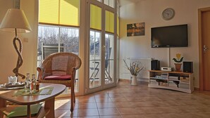 Ein Wohnzimmer mit einem großen Fenster, einem Fernseher und einem Korbsessel.