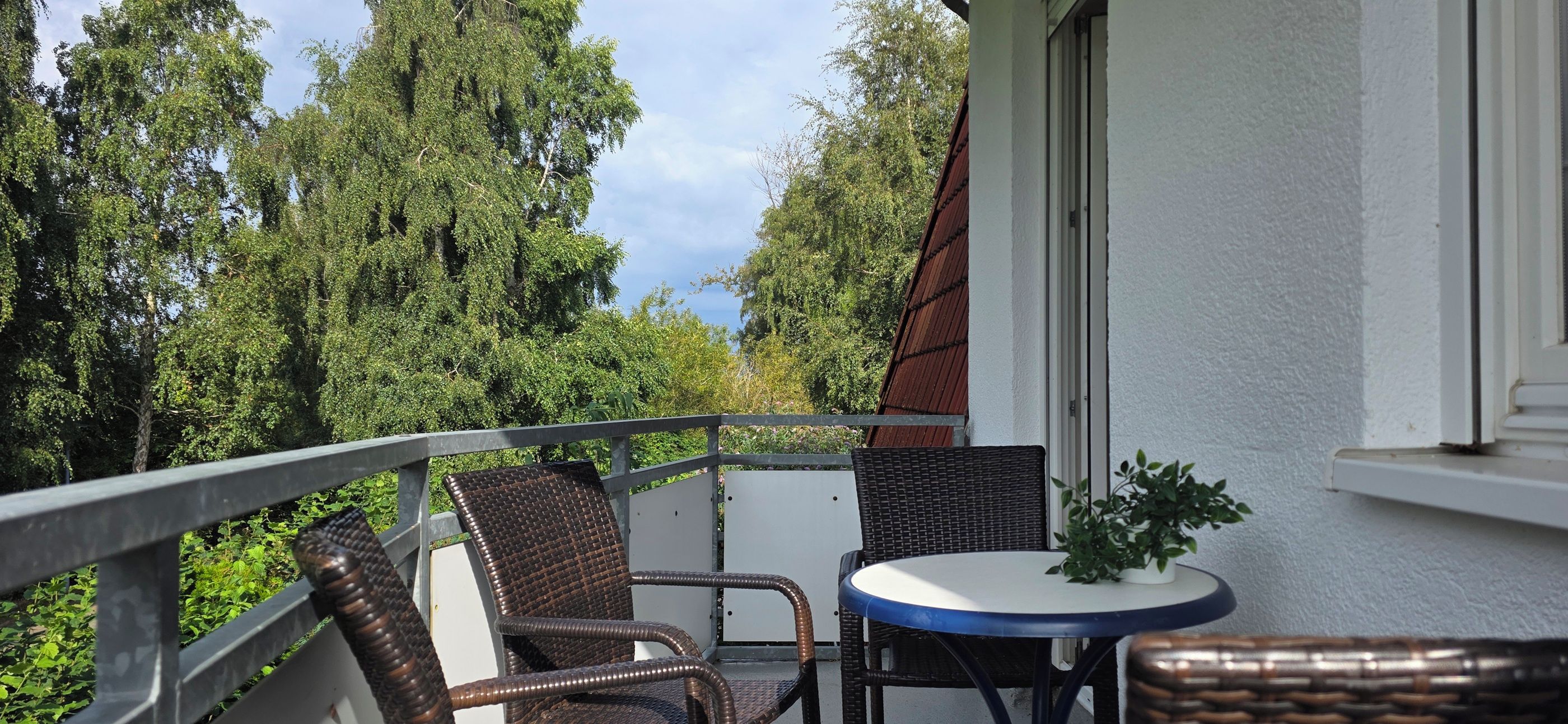 Un balcon agrémenté de meubles en osier, d’une petite table et d’une plante en pot.