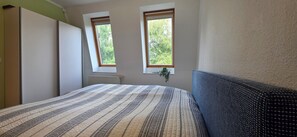 Una camera da letto con un letto, due finestre, un termosifone e una pianta.