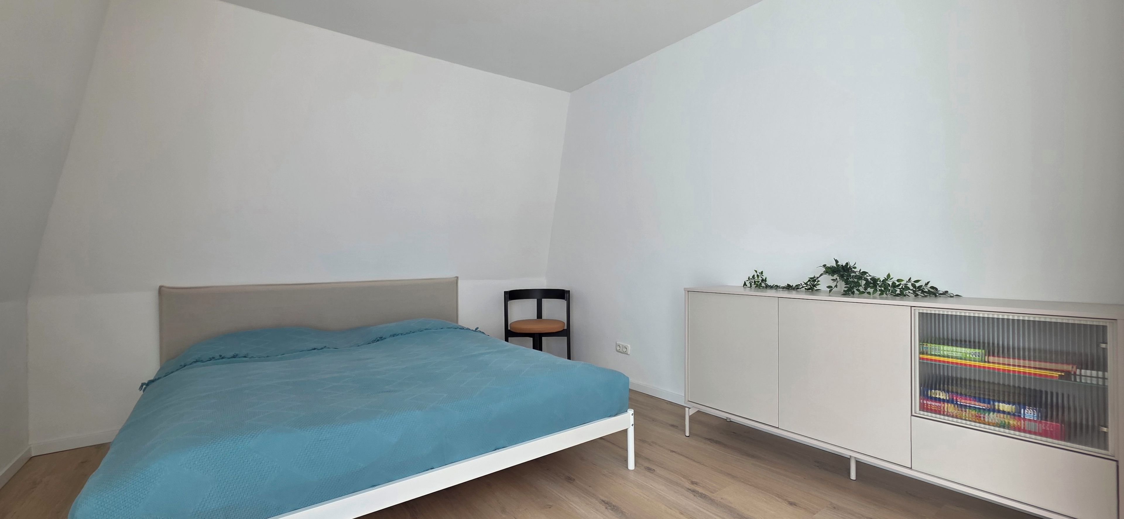 A bedroom with a bed, a chair, and a white wardrobe.