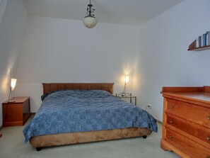 Quarto com cama, mesas de cabeceira, cómoda e luminária no teto.
