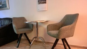 Ein kleiner Raum mit einem runden Tisch, zwei Stühlen, einem schwarzen Ledersofa und einem gerahmten Bild an der Wand.